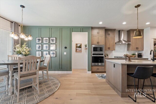203 S Fusion Ave, Kuna, ID 83634 - kitchen with appliances with stainless steel finishes, wall chimney exhaust hood, light wood-style flooring, light countertops, and a decorative wall