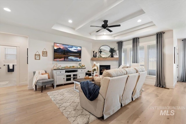 203 S Fusion Ave, Kuna, ID 83634 - living room with light wood-type flooring, a ceiling fan, a raised ceiling, recessed lighting, and a lit fireplace