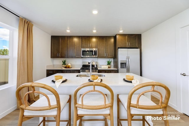 kitchen featuring appliances with stainless steel finishes, a sink, light countertops, dark brown cabinets, and light wood finished floors