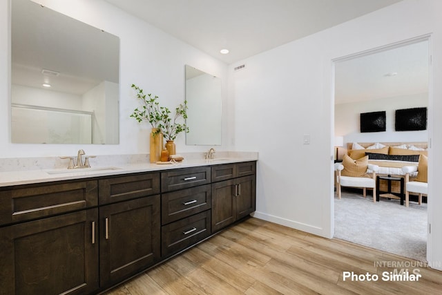 bathroom with wood finished floors, double vanity, baseboards, connected bathroom, and a shower with shower door