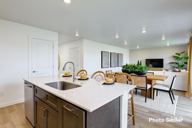 kitchen featuring a sink, light wood-style floors, recessed lighting, dishwasher, and a breakfast bar