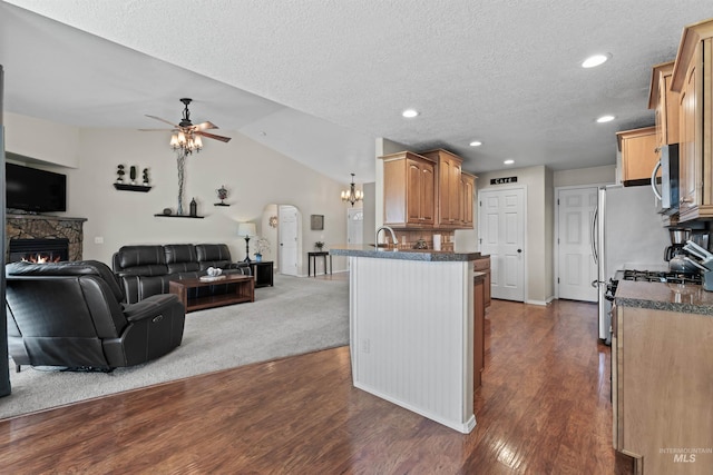 kitchen featuring open floor plan, stainless steel microwave, a ceiling fan, a stone fireplace, and a textured ceiling