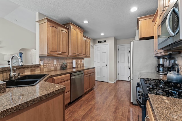 kitchen with stainless steel appliances, a sink, dark wood-type flooring, tile counters, and tasteful backsplash