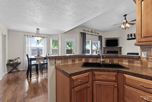 kitchen with a sink, dark wood-type flooring, brown cabinets, a textured ceiling, and dark countertops