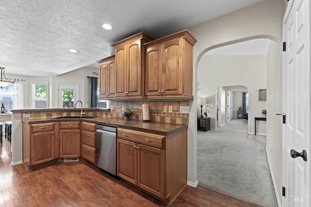 kitchen featuring stainless steel dishwasher, arched walkways, a sink, a peninsula, and a textured ceiling