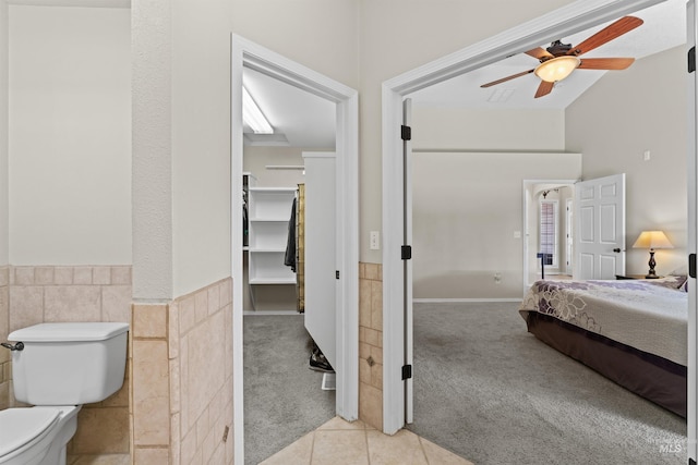 ensuite bathroom with a ceiling fan, toilet, tile walls, vaulted ceiling, and tile patterned flooring