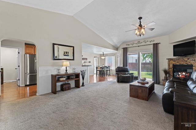 living area with light carpet, a ceiling fan, lofted ceiling, arched walkways, and a fireplace