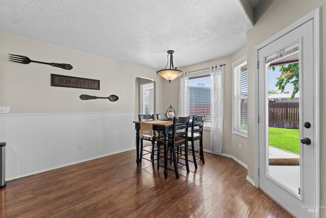 dining space with arched walkways, wood finished floors, a textured ceiling, plenty of natural light, and wainscoting