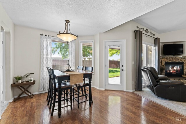 dining room with a stone fireplace, wood finished floors, a textured ceiling, arched walkways, and baseboards