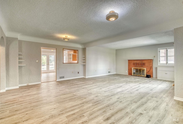 unfurnished living room with a fireplace, a textured ceiling, and light wood-type flooring