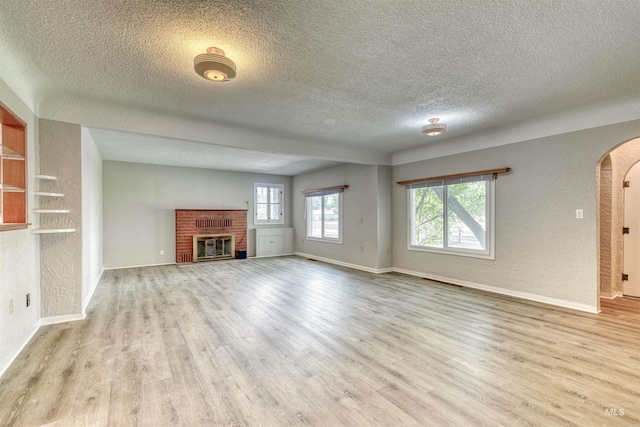 unfurnished living room with a healthy amount of sunlight, light hardwood / wood-style floors, a textured ceiling, and a brick fireplace