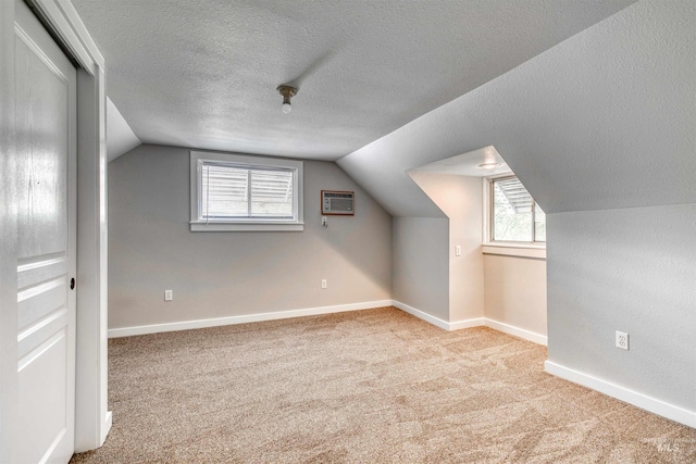 bonus room featuring an AC wall unit, a textured ceiling, light carpet, and vaulted ceiling