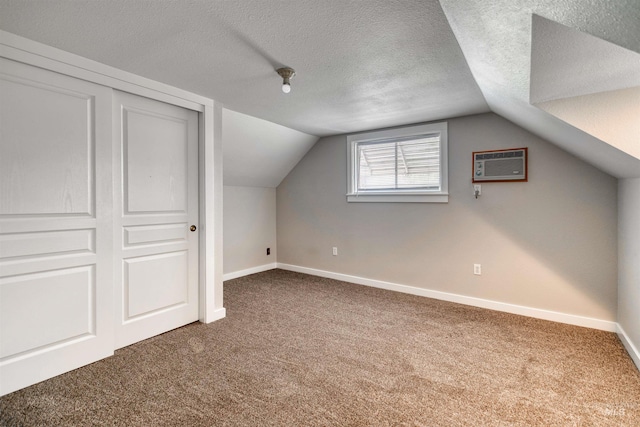 additional living space with a textured ceiling, carpet floors, a wall unit AC, and vaulted ceiling