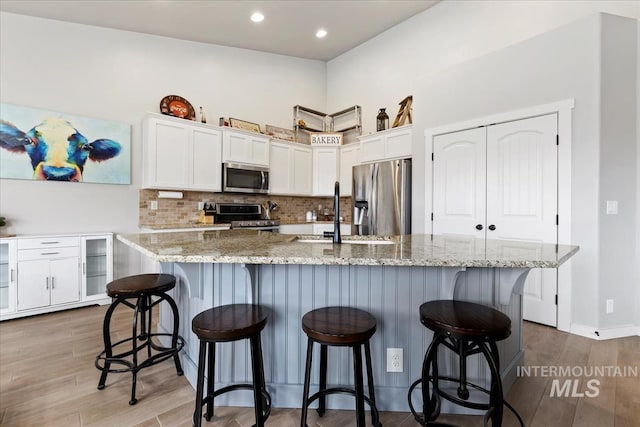 kitchen with a kitchen island with sink, hardwood / wood-style floors, a kitchen bar, sink, and appliances with stainless steel finishes