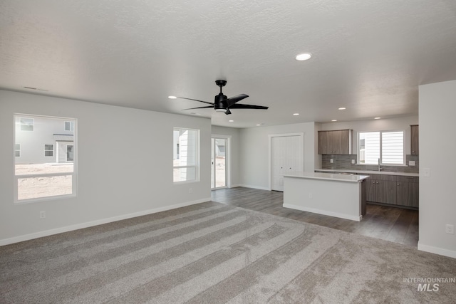 unfurnished living room with a textured ceiling, recessed lighting, a sink, a ceiling fan, and baseboards