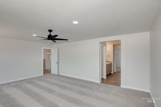 carpeted spare room featuring a textured ceiling, a ceiling fan, and baseboards