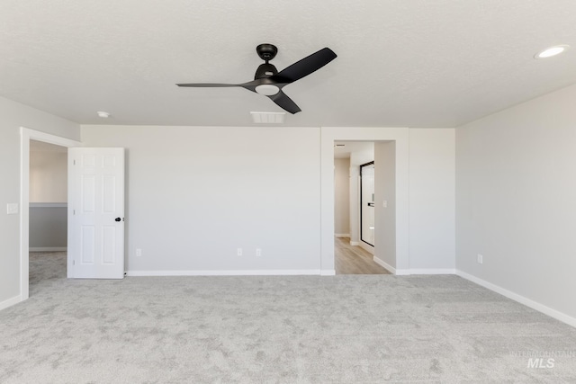 carpeted empty room featuring a textured ceiling, visible vents, a ceiling fan, and baseboards