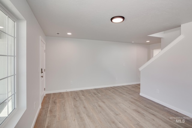 below grade area with light wood-style floors, baseboards, a textured ceiling, and recessed lighting