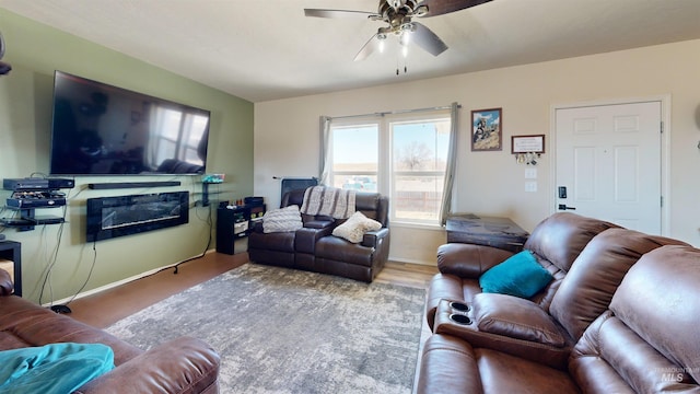 living area featuring a glass covered fireplace, a ceiling fan, and baseboards