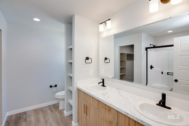bathroom with toilet, wood finished floors, a stall shower, and a sink