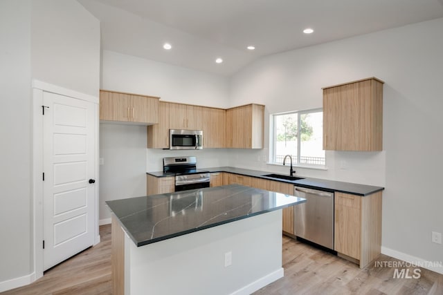 kitchen with light brown cabinets, a sink, a kitchen island, dark countertops, and stainless steel appliances