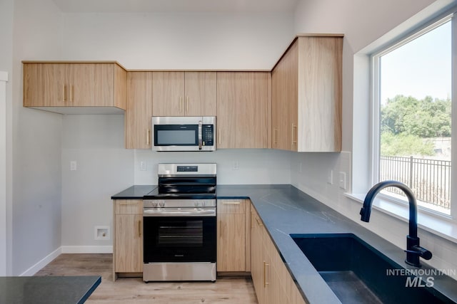 kitchen with a sink, light brown cabinets, dark countertops, and appliances with stainless steel finishes