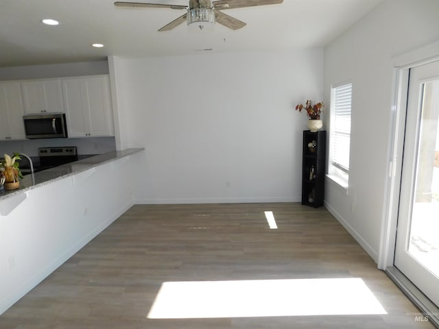 kitchen featuring appliances with stainless steel finishes, light hardwood / wood-style flooring, stone countertops, ceiling fan, and white cabinetry