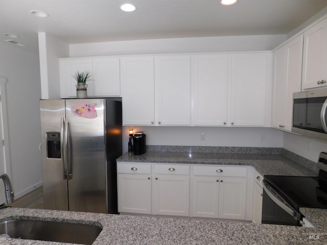 kitchen featuring white cabinets, stainless steel appliances, dark stone counters, and sink