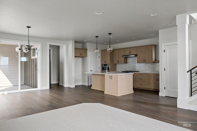 kitchen featuring dark hardwood / wood-style floors, an island with sink, hanging light fixtures, and tasteful backsplash