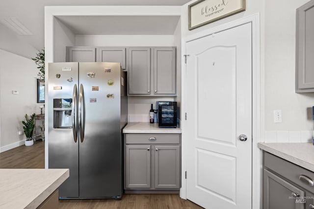 kitchen with stainless steel refrigerator with ice dispenser, hardwood / wood-style flooring, and gray cabinetry