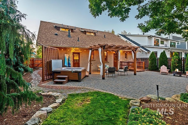 back of property with a hot tub, a pergola, and a patio area