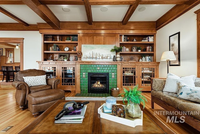 living room featuring built in shelves, coffered ceiling, wood-type flooring, beamed ceiling, and a tiled fireplace