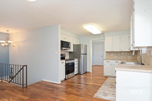 kitchen featuring a sink, an inviting chandelier, appliances with stainless steel finishes, white cabinets, and light countertops