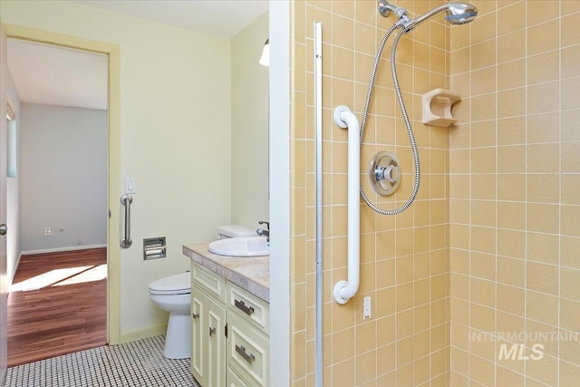 bathroom featuring tile patterned flooring, baseboards, toilet, a tile shower, and vanity