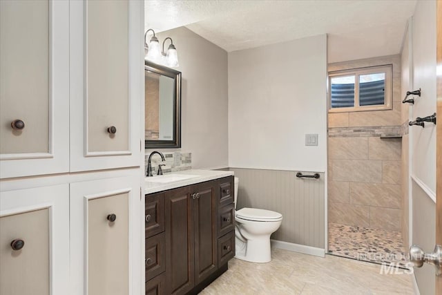 bathroom with walk in shower, a wainscoted wall, toilet, vanity, and a textured ceiling