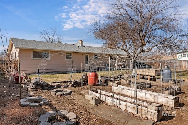 rear view of house with a chimney, an outdoor fire pit, and a garden