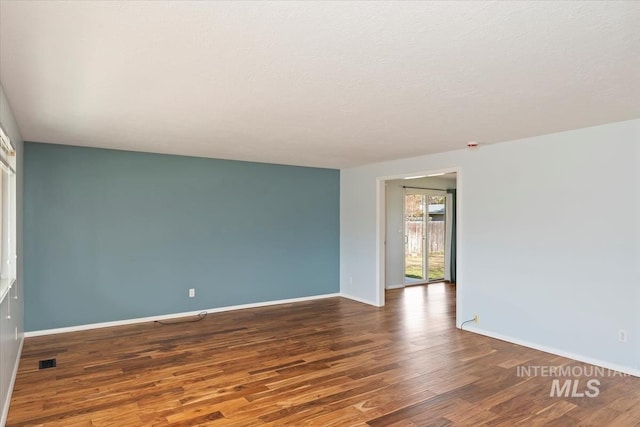 unfurnished room with visible vents, a textured ceiling, baseboards, and wood finished floors