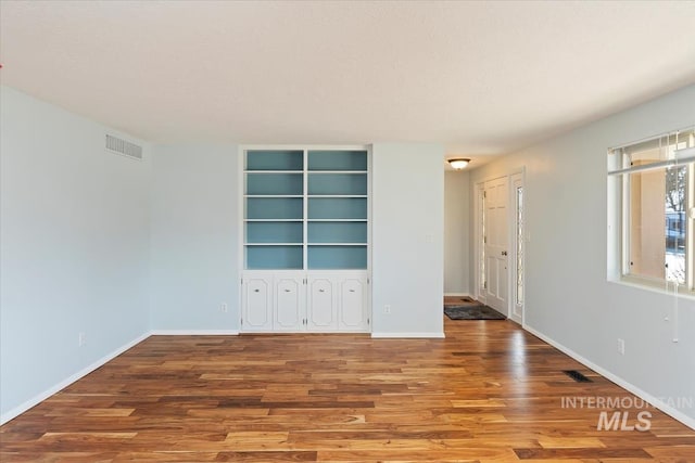 unfurnished room featuring visible vents, baseboards, and wood finished floors