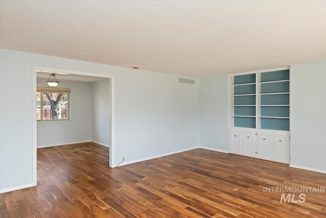 unfurnished room featuring visible vents, a textured ceiling, baseboards, and wood finished floors