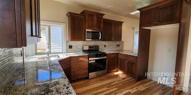 kitchen featuring light stone counters, backsplash, stainless steel appliances, and light wood-type flooring