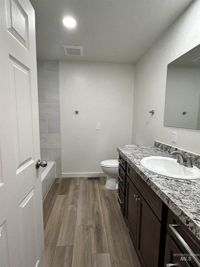 bathroom featuring vanity, wood finished floors, visible vents, baseboards, and toilet