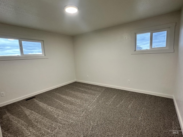 unfurnished room featuring visible vents, baseboards, and dark carpet