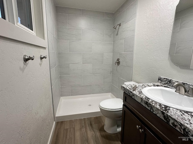 bathroom featuring a textured wall, toilet, wood finished floors, and a tile shower