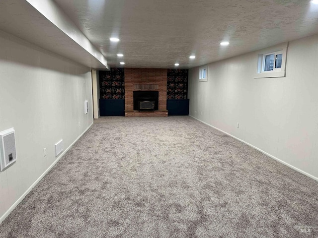 finished basement with visible vents, a brick fireplace, baseboards, carpet flooring, and a textured ceiling