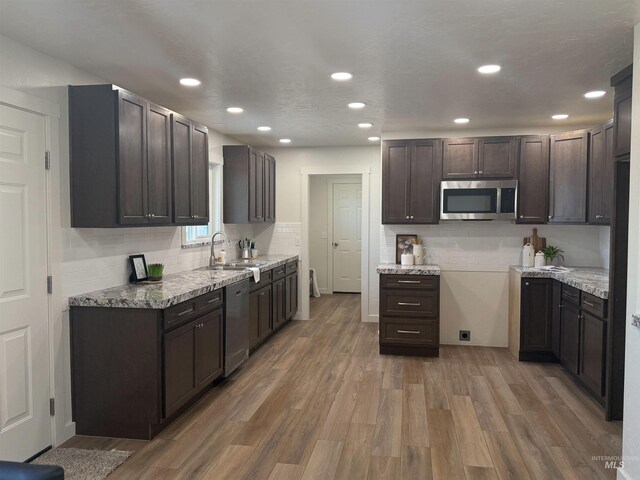 kitchen with a sink, dark brown cabinets, light wood-style floors, appliances with stainless steel finishes, and tasteful backsplash