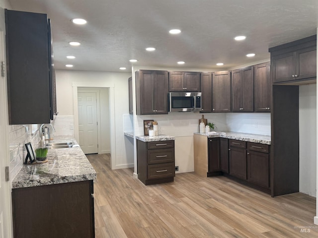 kitchen featuring recessed lighting, a sink, dark brown cabinetry, stainless steel microwave, and light wood-type flooring