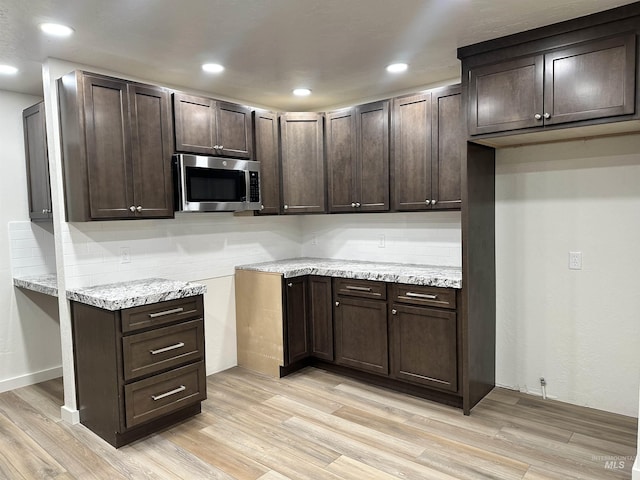 kitchen featuring light wood-style floors, stainless steel microwave, dark brown cabinetry, and backsplash