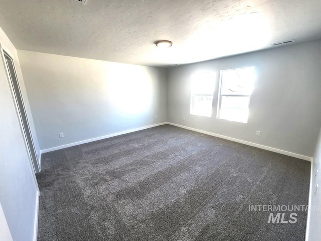 empty room featuring a textured ceiling and dark colored carpet