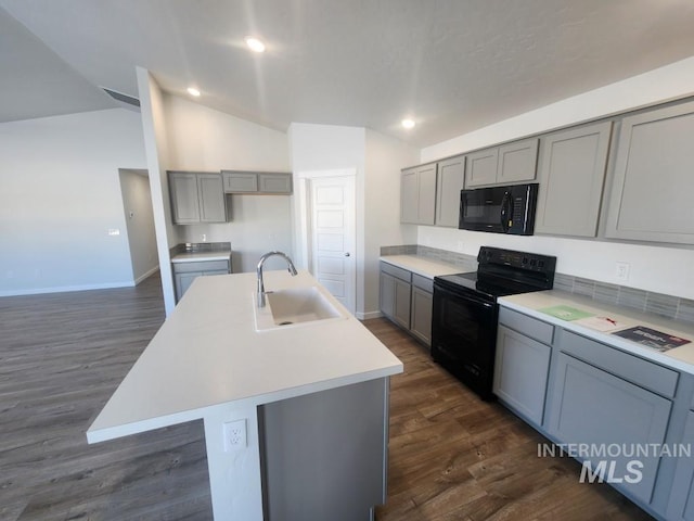 kitchen with sink, lofted ceiling, gray cabinets, a center island with sink, and black appliances