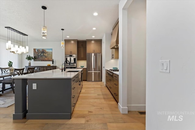 kitchen featuring light wood-style flooring, hanging light fixtures, stainless steel appliances, light countertops, and a sink